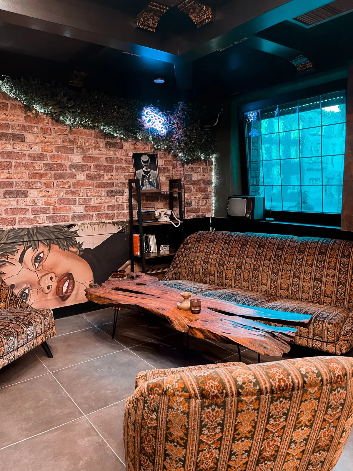 Loungeecke mit gemustertem Vintage-Sofa, Baumkantentisch, Backsteinwand und Neonschriftzug